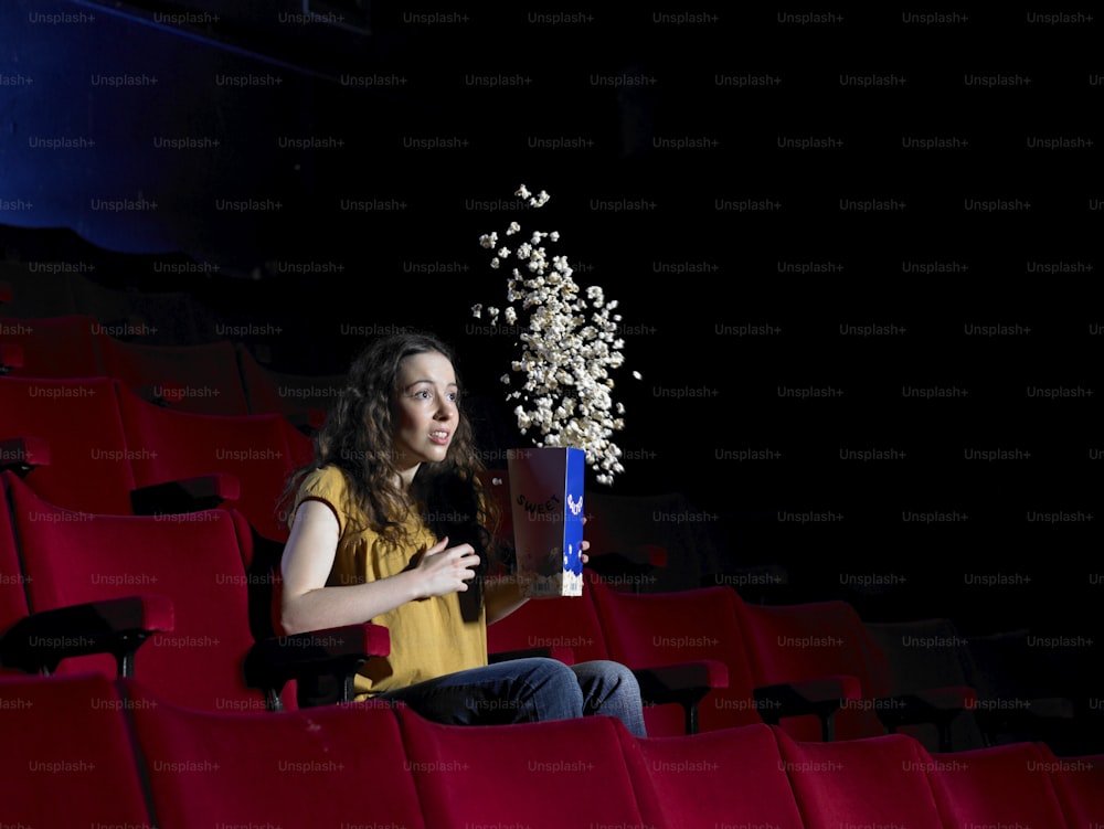 a woman sitting in a theater holding a box of popcorn