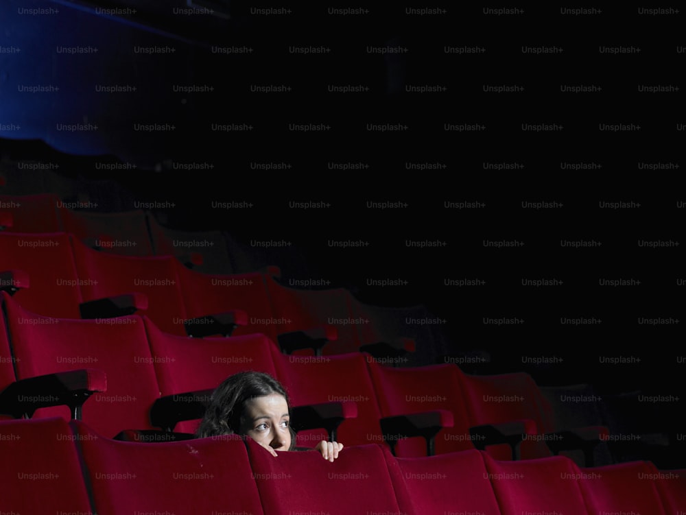 a woman peeking out from behind a row of red chairs