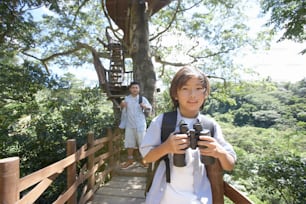 a young boy holding a camera while standing on a bridge