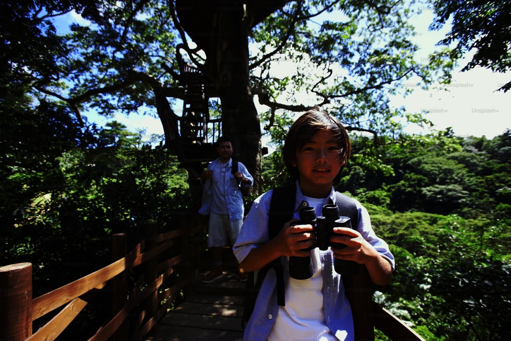 a young boy holding a camera while standing on a bridge
