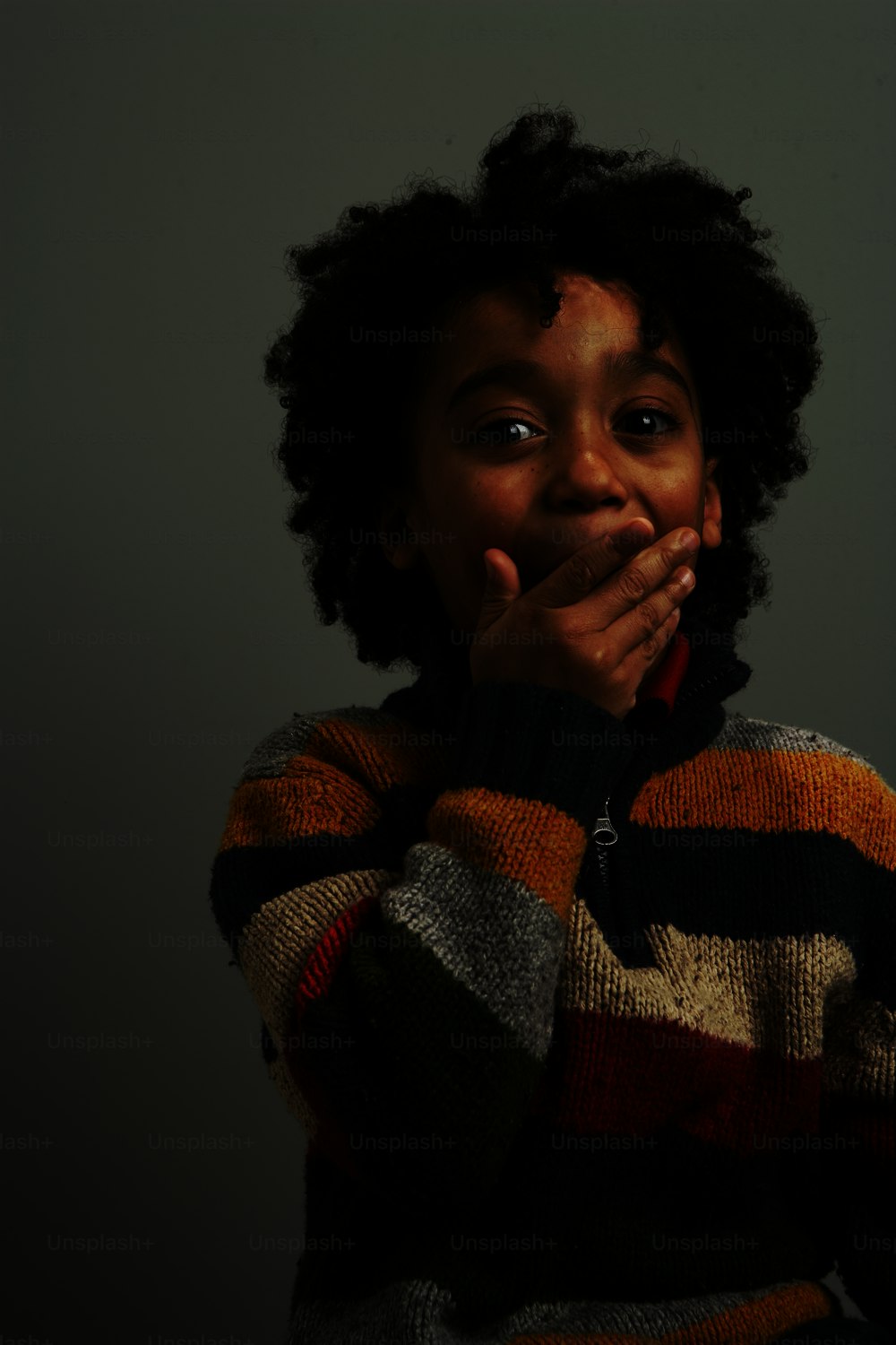 a young boy covers his mouth with his hands