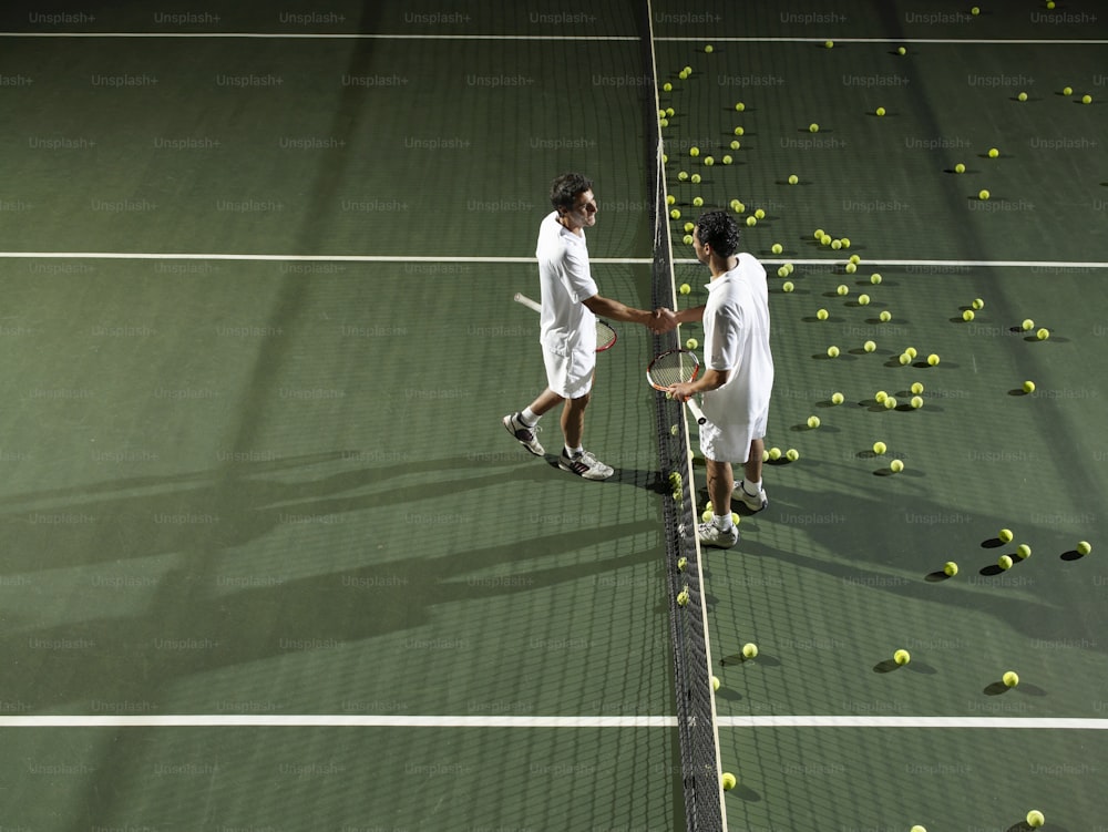 Zwei Tennisspieler schütteln sich die Hände �über einen Schläger