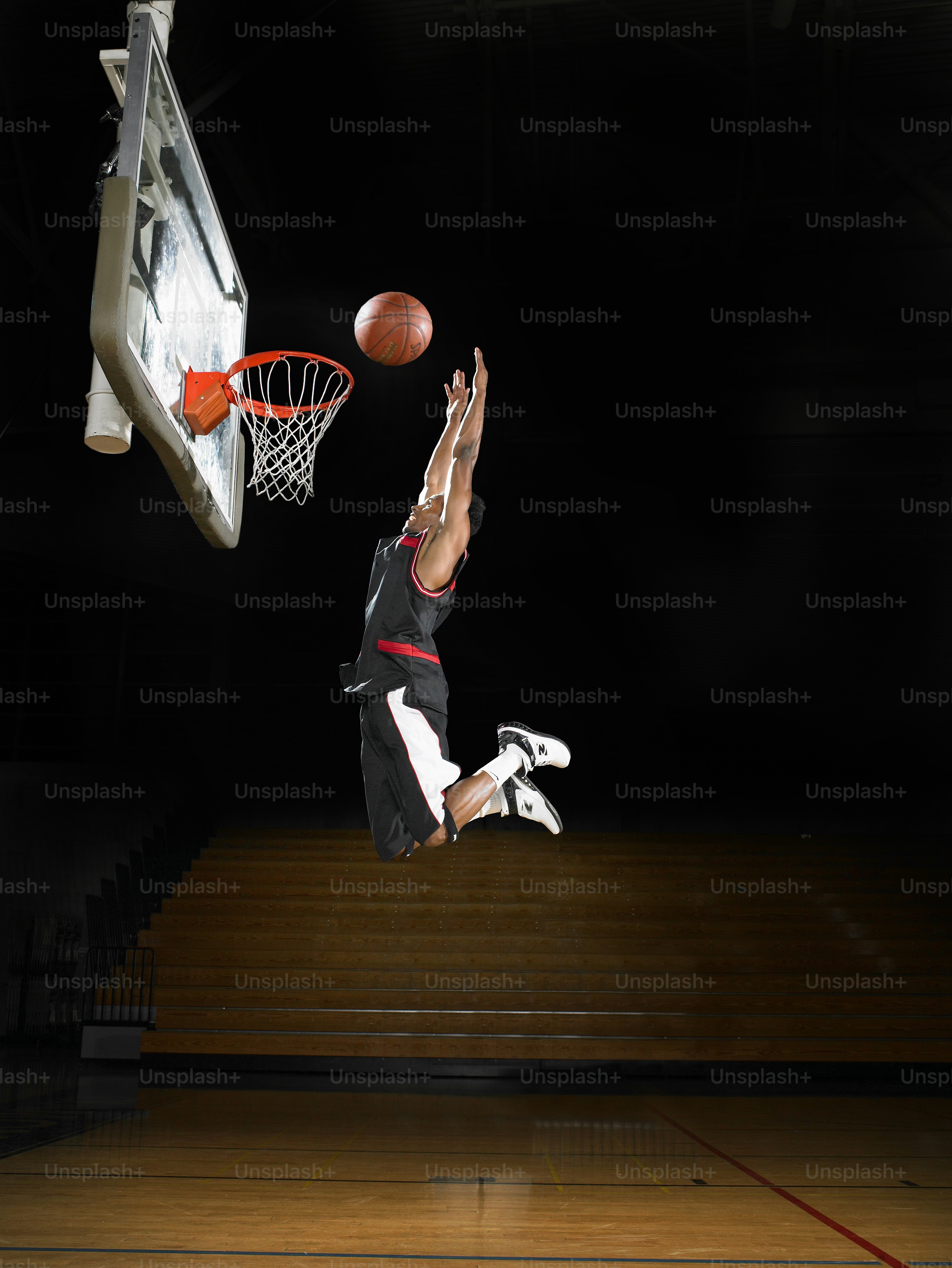 A basketball player elevates toward the rim in an empty gym, frozen midair beneath the hoop.
