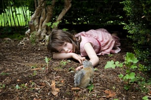 a little girl laying on the ground next to a squirrel
