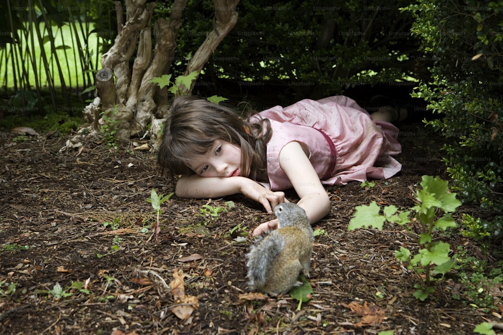 a little girl laying on the ground next to a squirrel