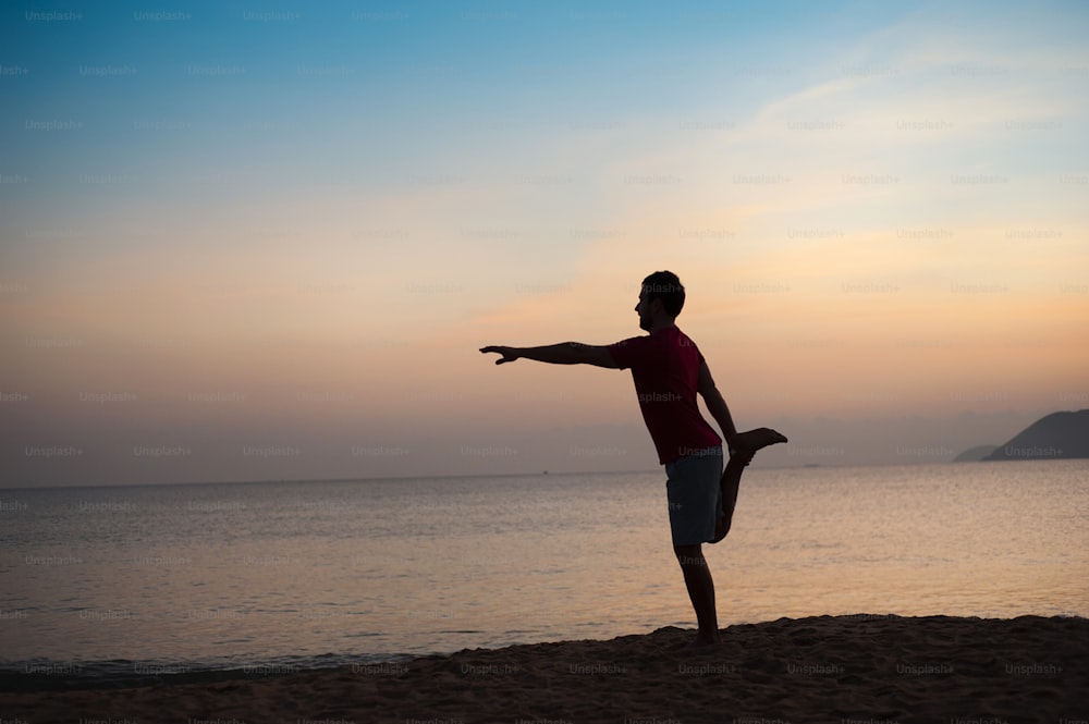 Silhouette dell'uomo sportivo attivo che corre ed esercita sulla spiaggia al tramonto.