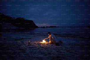 a man sitting on a beach next to a fire