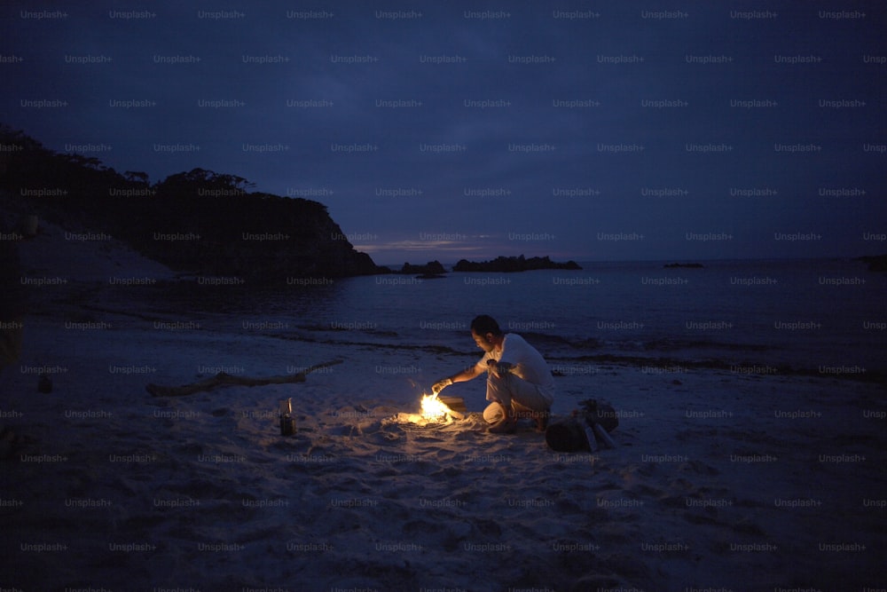 a man sitting on a beach next to a fire
