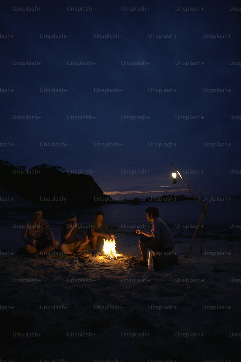 a group of people sitting around a fire on a beach