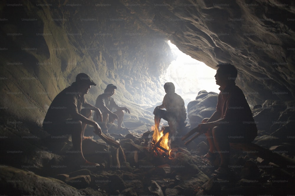 um grupo de pessoas sentadas ao redor de um incêndio em uma caverna