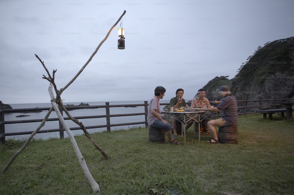 um grupo de pessoas sentadas ao redor de uma mesa em cima de um campo coberto de grama