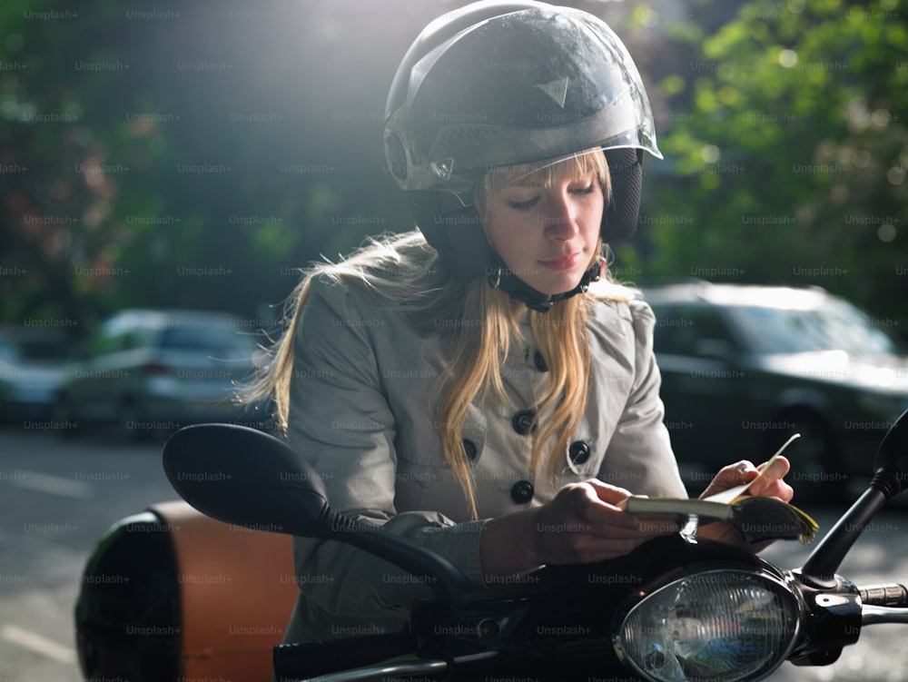 a woman sitting on a motorcycle writing on a piece of paper