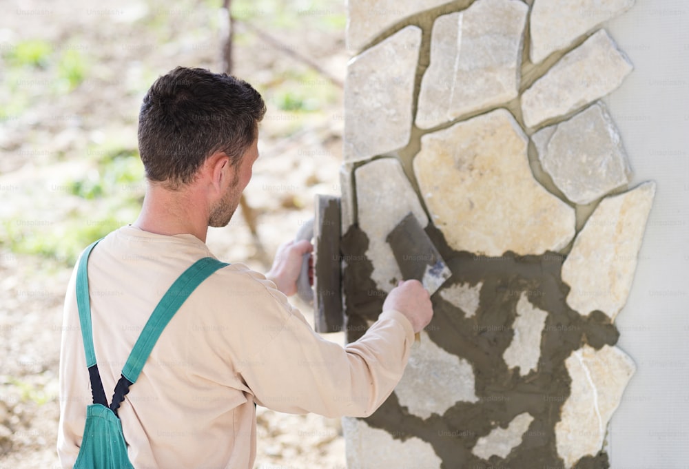 Albañil colocando piedras naturales decorativas en una pared
