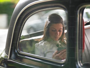 Una mujer sentada en un auto mirando su teléfono celular