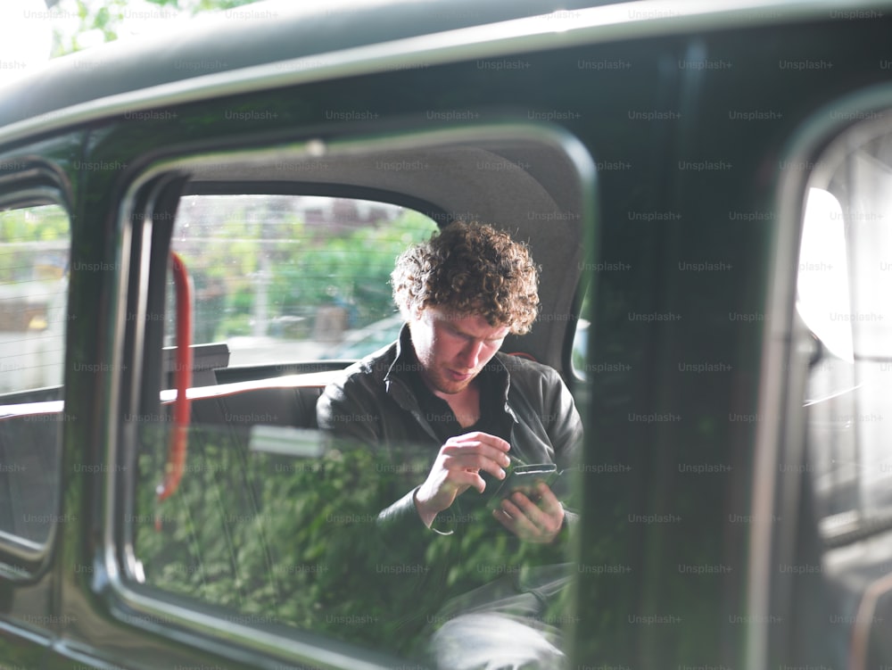 Un homme assis dans une voiture regardant son téléphone portable