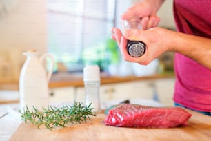 Ungrcognizable man in the kitchen preparing beef steak