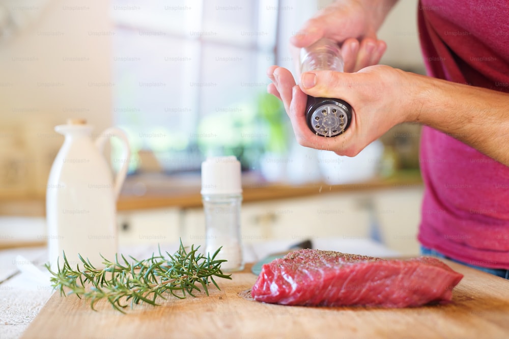 Ungrcognizable man in the kitchen preparing beef steak