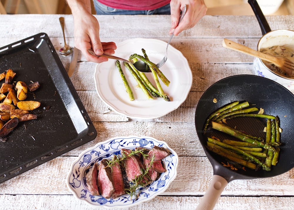 Man serving grilled beef steak, asparagus and baked potatoes
