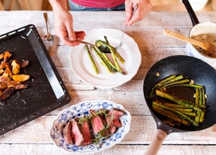 Man serving grilled beef steak, asparagus and baked potatoes