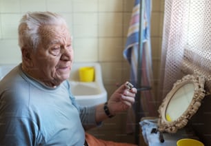 Senior man shaving his beard in bathroom in front of the mirror