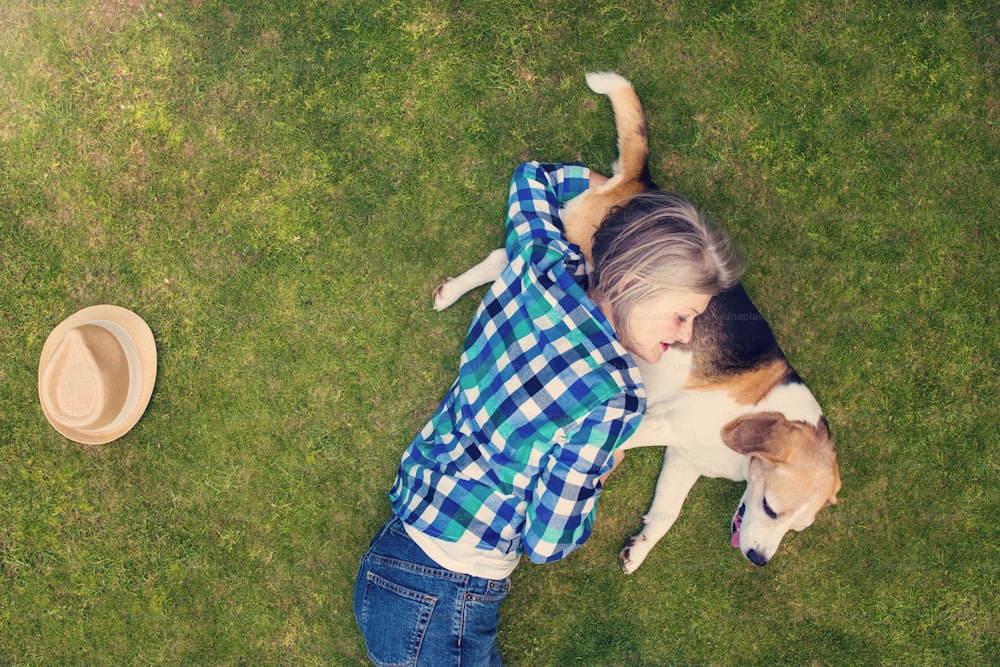 Beautiful senior woman with a dog lying on a grass