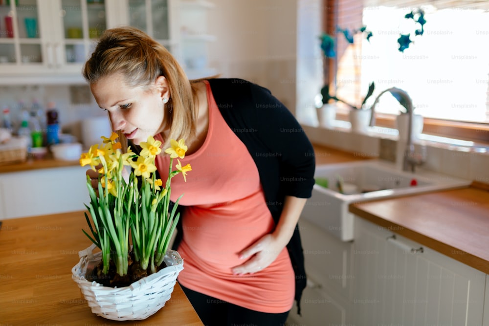Pregnant woman taking care of flowers in modern kitchen