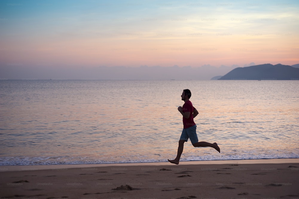 夕暮れ時にビーチで走ったり運動したりするスポーツアクティブな男性のシルエット。