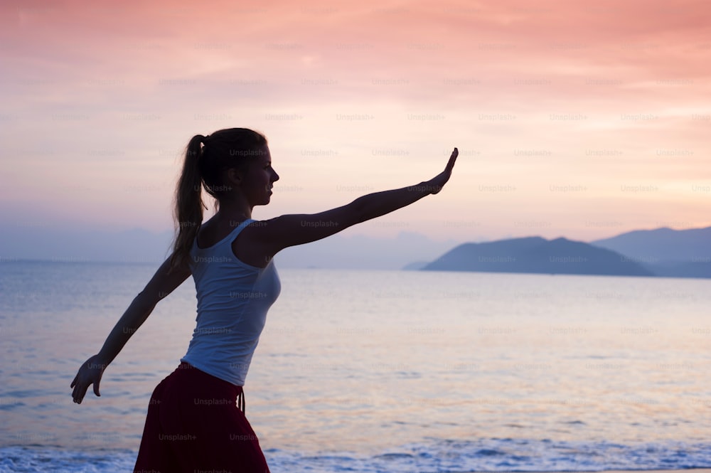 Silhueta da mulher ativa do esporte se alongando e se exercitando na praia ao pôr do sol.