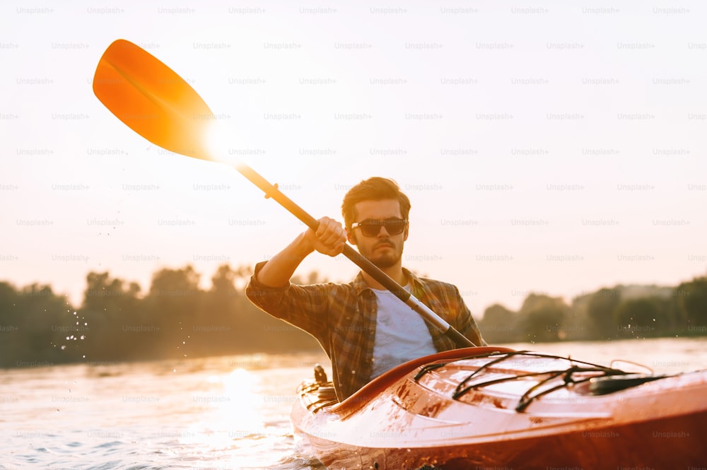 Bel giovane in kayak sul fiume con il tramonto sullo sfondo