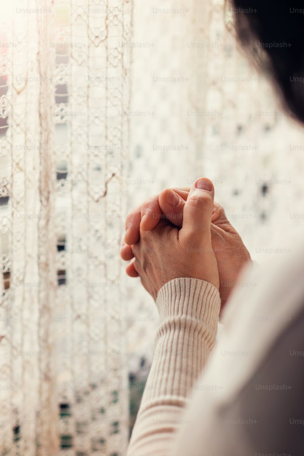 Hands of an unrecognizable woman standing by the window and praying