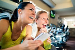 Two attractive fit women in a gym during a break with smart phone laughing