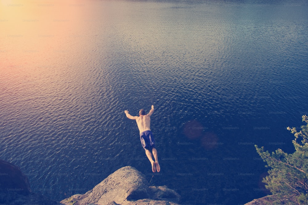 Young man jumping into the river from cliff (man in motion blur, intentional sun glare and vintage color)