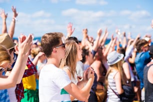 Adolescentes en el festival de música de verano debajo del escenario en una multitud que se divierte, con el brazo levantado