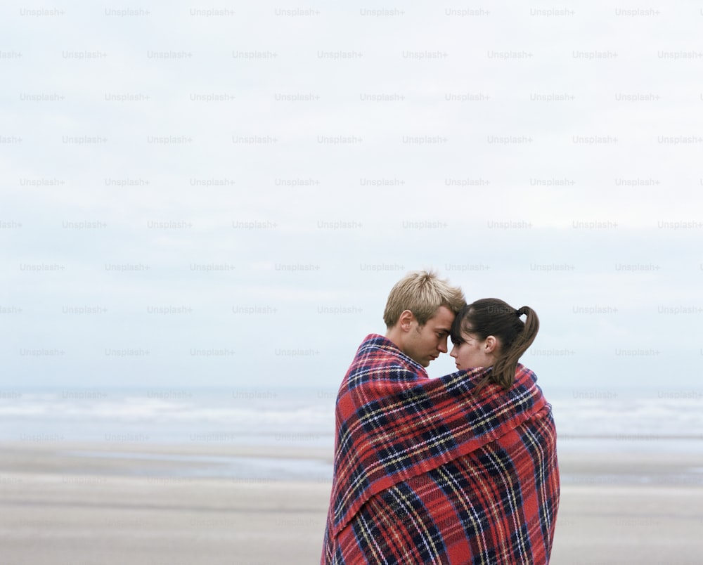 a man and woman wrapped in a blanket on the beach