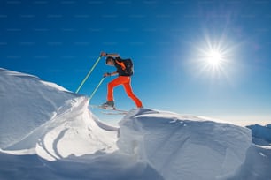Un uomo di sci alpino si arrampica su sci e pelli di foca in tanta neve con ostacoli in una giornata di sole forte