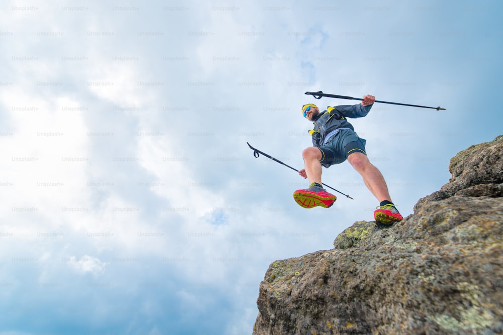Male athlete falls over a cliff with sticks while practical training at the mountain trail