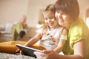 Grandmother and granddaughter laying on the floor and using tablet.