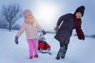 Two cute girls pulling his brother on a sled.