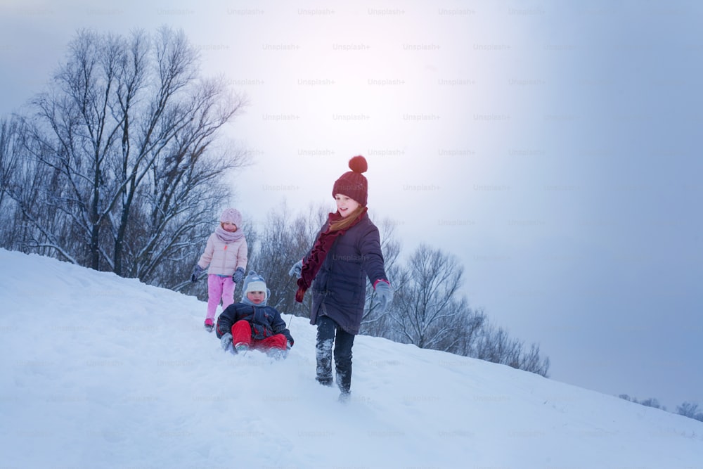 Two cute girls pulling his brother on a sled. Space for copy.