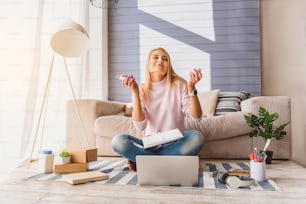 This scent is wonderful. Carefree girl is smelling perfume and smiling. Her eyes are closed with pleasure. Lady is sitting on floor near laptop