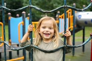 Little girl is climbing at the playground and looking at camera.