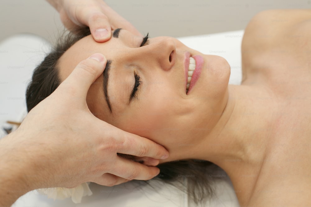 Esthéticienne massant la tête et le visage d’une jeune femme pendant le soin du visage.