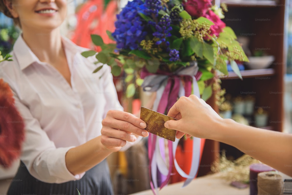 Primer plano de la mano femenina que da la tarjeta de crédito a la vendedora. El florista sostiene un ramo y sonríe