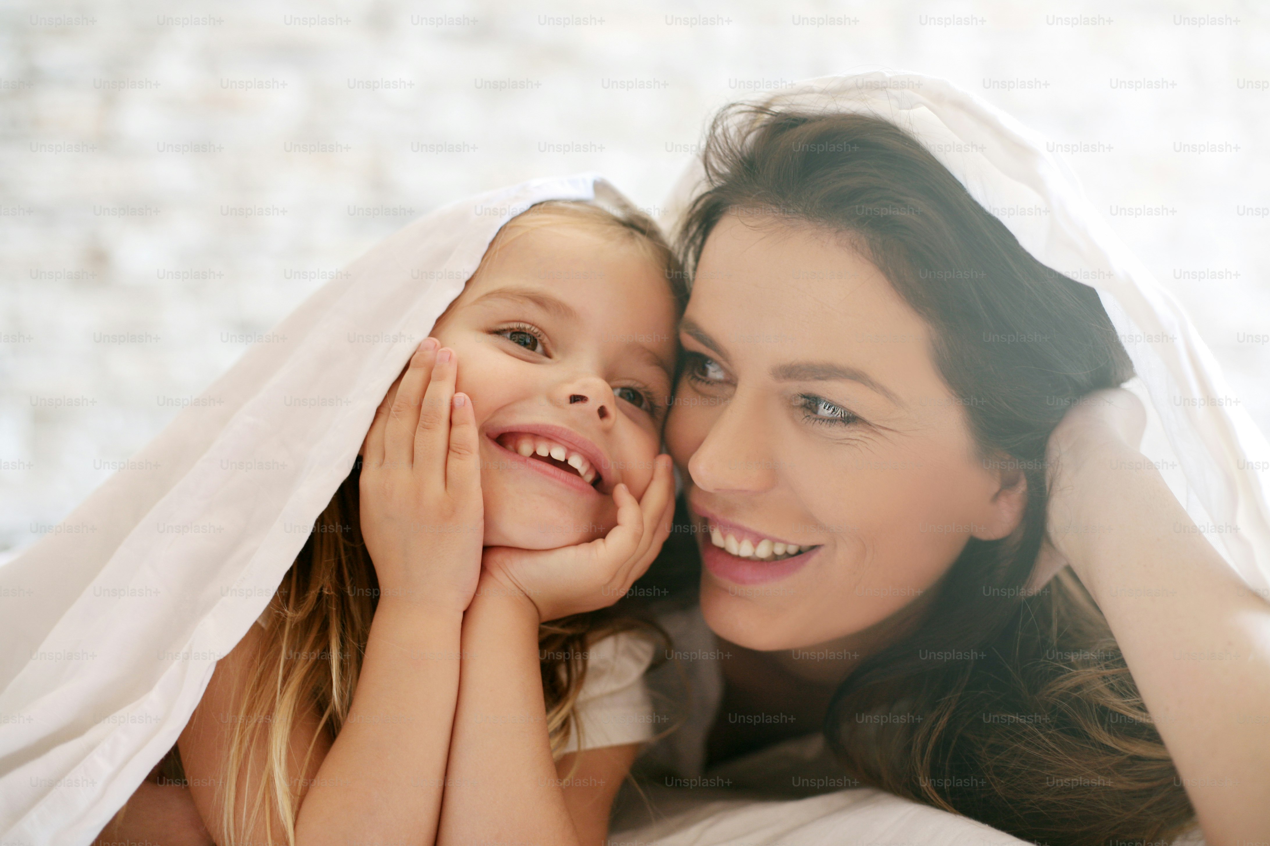 Ibu dan anak perempuan yang bahagia di bawah selimut.