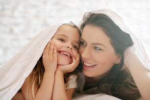Happy mother and daughter under blanket.