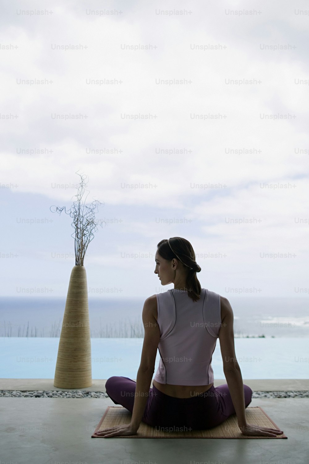 a woman sitting on a yoga mat in front of a body of water