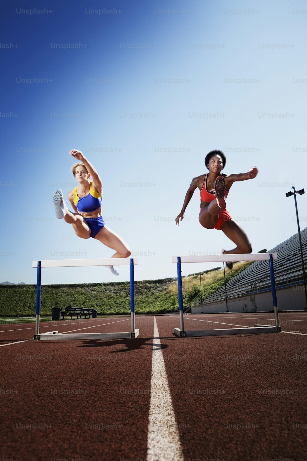 two women jumping over a hurdle on a track