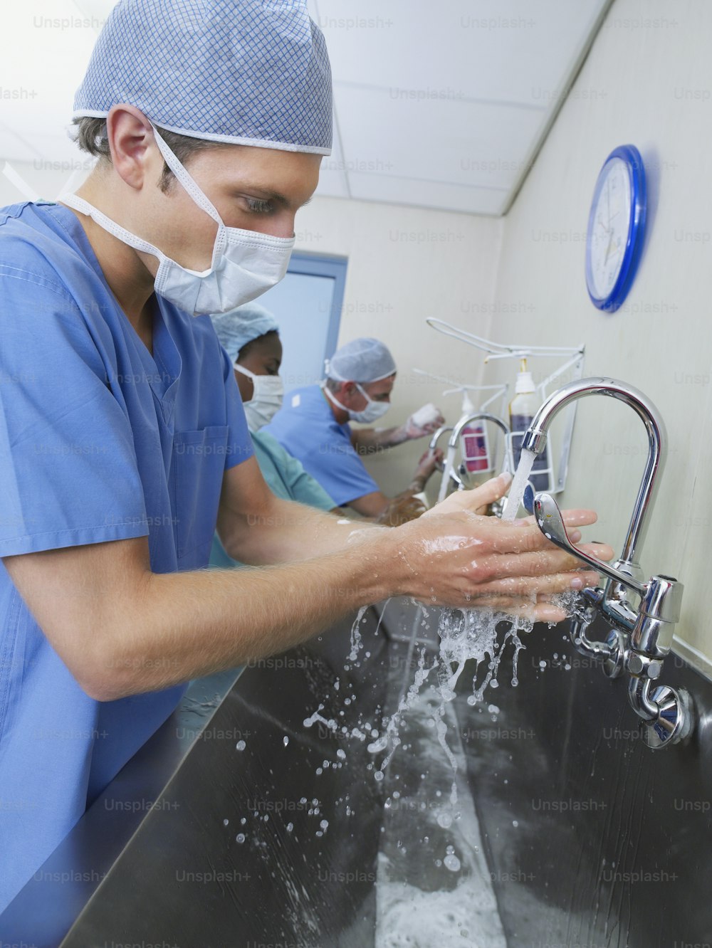 a man in scrubs washing his hands in a sink