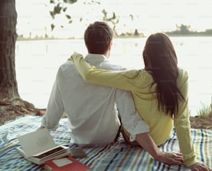 a man and woman sitting on a blanket next to a lake