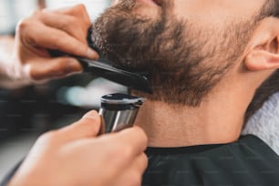 Nahaufnahme von Friseurhänden, die den männlichen Bart mit einem speziellen Elektrorasierer schneiden und genau kämmen